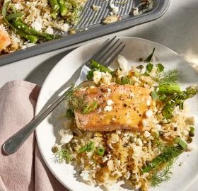 Ein Teller mit gebratenem Lachs, Reis, Spargel und frischen Kräutern, serviert mit einer Gabel. Gesundes und schmackhaftes Gericht.